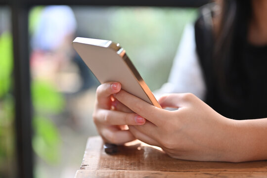 Cropped image of a woman's hands using a smartphone over a wooden working desk.