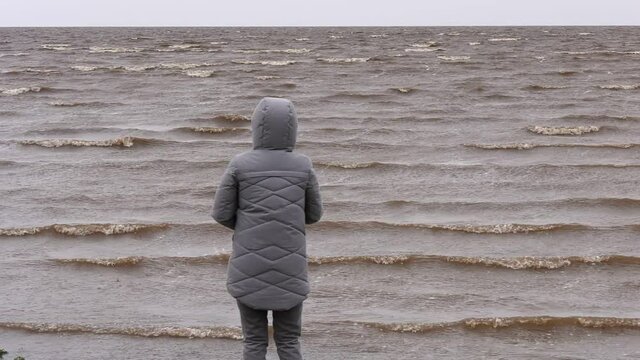 Woman Throwing Stones in Water. Windy Autumn Day at the Shore of Lake Ilmen. Back view