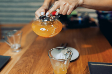 Woman's hand poured sea buckthorn honey tea from glass teapot into a cup of glass