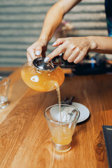 Woman's hand poured sea buckthorn honey tea from glass teapot into a cup of glass