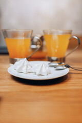 Two cups of sea buckthorn tea on the table and two marshmallows on a plate