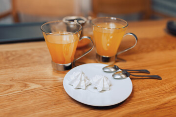 Two cups of sea buckthorn tea on the table and two marshmallows on a plate