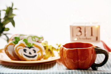 Happy Halloween still life with pumpkin cup and homemade cookies in shape of cute pumpkins and date of Halloween Day. Atmospheric aesthetic autumn holiday concept. Rural life