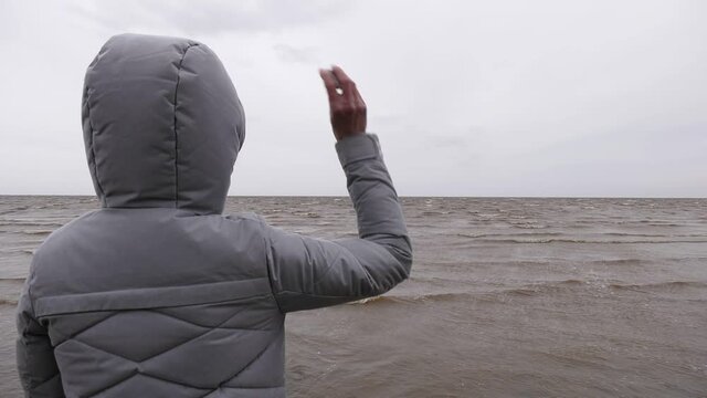 Woman Throwing Stones in Water. Windy Autumn Day at the Shore of Lake Ilmen. Back view