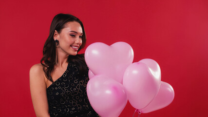 flattered woman in black dress holding pink balloons isolated on red.