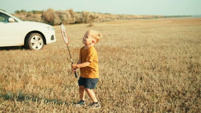 Smiling child walking with a badminton racket in his hands in nature