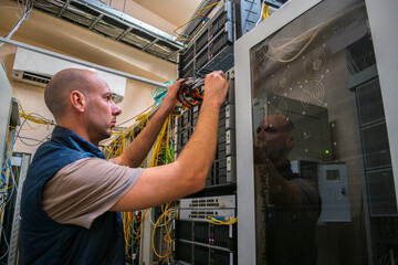 An engineer connects the fiber optic cable to the switch's network interface. A man works in a data center server rack. Maintenance of computer equipment of an Internet provider.