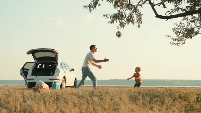 Cheerful happy father and son throwing a soccer ball to each other in nature