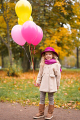 Small girl walking in the autumn park with colourful balloons
