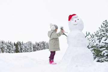 child builds a snowman in the winter in the yard. concept of winter games with snow for children