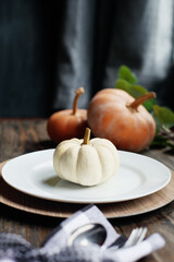 Holiday place setting with plate, napkin, and silverware on a Thanksgiving Day decorated table. White and Orange pumpkins. Selective focus with blurred foreground and background. 