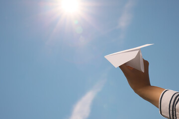 Woman holding paper plane against blue sky, closeup. Space for text