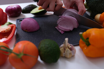 Chef cutting red onion on board among vegetables closeup