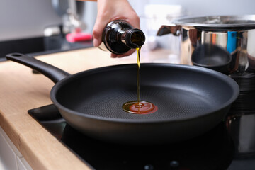Chef pouring olive oil into frying pan in kitchen closeup