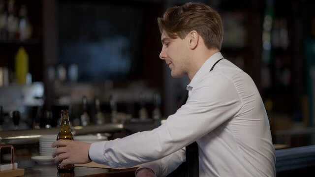 Stressed angry businessman loosing necktie unbuttoning shirt drinking beer sitting at bar counter. Side view of troubled Caucasian young man having problems thinking with alcohol indoors