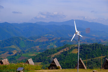Beautiful mountain scenery with windmills, huts, flowers, and solar panels foreground.