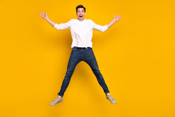 Fototapeta na wymiar Full body photo of impressed brunet young guy jump wear shirt jeans sneakers isolated on yellow background