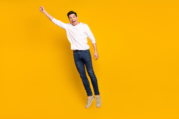 Fototapeta na wymiar Full size photo of funky brunet millennial guy jump wear shirt jeans sneakers isolated on yellow background