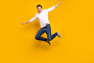 Full body photo of funny brunet young guy jump wear shirt jeans sneakers isolated on yellow background