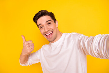 Photo of funky brunet young guy do selfie show thumb up wear shirt isolated on yellow background