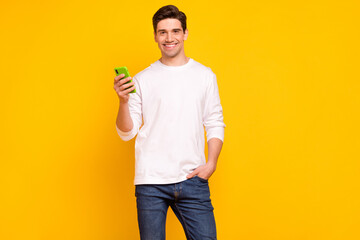 Photo portrait young man using cellphone browsing internet wearing jeans isolated bright yellow color background
