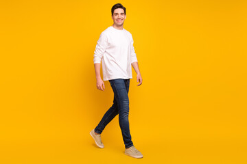 Full body profile photo of cute brunet millennial guy go wear shirt jeans sneakers isolated on yellow color background