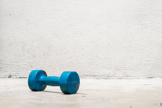 blue dumbbell on the ground (used, dusty and abandoned) white background, exercise at home, space for text. exercise and health concept. fitness concept