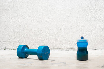 blue dumbbell and bottle with water on the floor (used, dusty and abandoned) white background, exercise at home, space for text. exercise and health concept. fitness concept