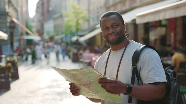 African man with paper map in hands staning on city street
