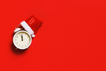 Alarm clock with a Christmas cap on a red background with copy space. New Years celebration concept.