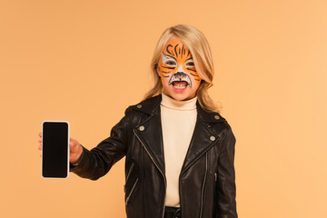 child with tiger face painting showing smartphone with blank screen and growling isolated on beige