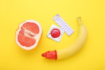Condom with pills in blister, banana and grapefruit on yellow background