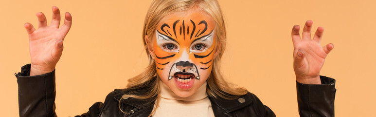 girl with tiger face painting growling and showing scary gesture isolated on beige, banner