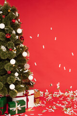 presents under decorated christmas tree and falling confetti on red