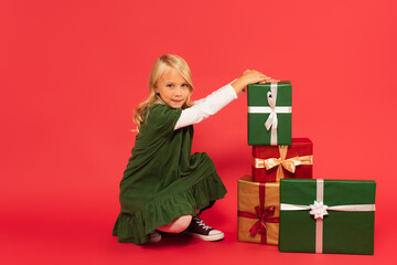 girl in green dress smiling at camera near stack of gift boxes on red