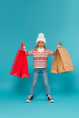 child in warm sweater, jeans and sneakers standing with shopping bags on blue