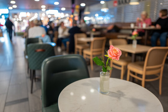 Pink rose on a ceramic table with people sitting at a table in a indoor restaurant