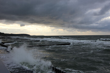 Storm clouds over the Baltic Sea, sunset view of waves and splashes from wooden breakwaters from the high shore