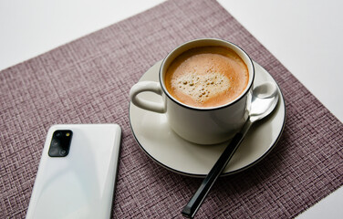 white mug with coffee,doughnut and a phone on a purple background. top view. breakfast