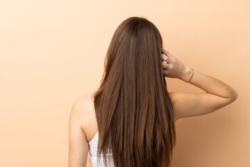 Young caucasian woman isolated on beige background in back position and thinking