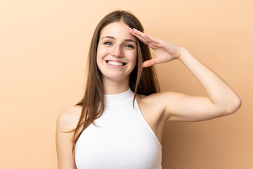 Fototapeta premium Young caucasian woman isolated on beige background saluting with hand with happy expression