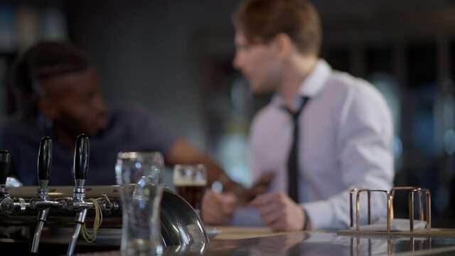 Blurred Caucasian man taking car key from bar counter as African American friend stops mate from drunken driving. Drunk male friends talking gesturing discussing danger and social responsibility