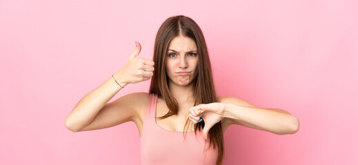 Young caucasian woman isolated on pink background making good-bad sign. Undecided between yes or not