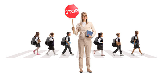 Female teacher holding a stop sign and schoolchildren crossing a street on a crosswalk