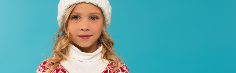 girl in knitted hat looking at camera isolated on blue, banner