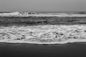 Panoramic view of the shore, the pacific ocean with waves, the horizon with cloudy sky and beach (in black and white)
