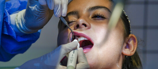 Young caucasian female with dentist in white latex gloves check condition of her teeth. baby girl in blue dental chair.