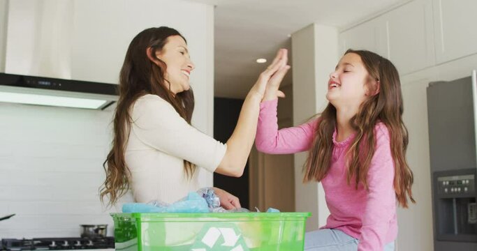 Happy caucasian mother and daughter segregating rubbish, giving high five