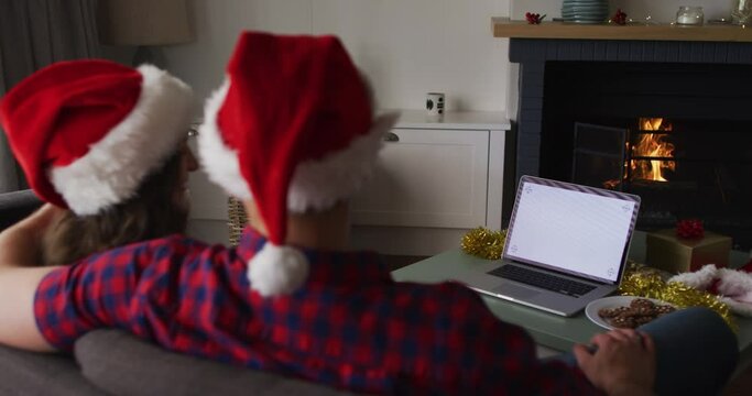 Back view of caucasian couple wearing santa hats using laptop with copy space on screen