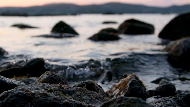 slow motion, a warm summer evening sunset on the shore of the mora through the strait, the sun almost went down behind the mountains, there are many stones on the near shore